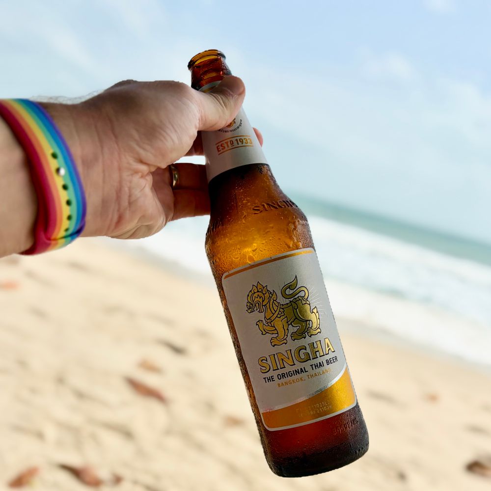 A bottle of Singha beer being held above the beach. 