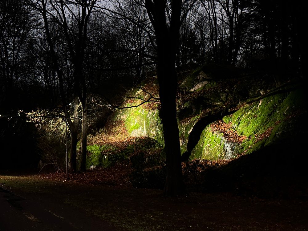 Valaistu sammaleinen kallion seinämä pimeässä puistossa.
