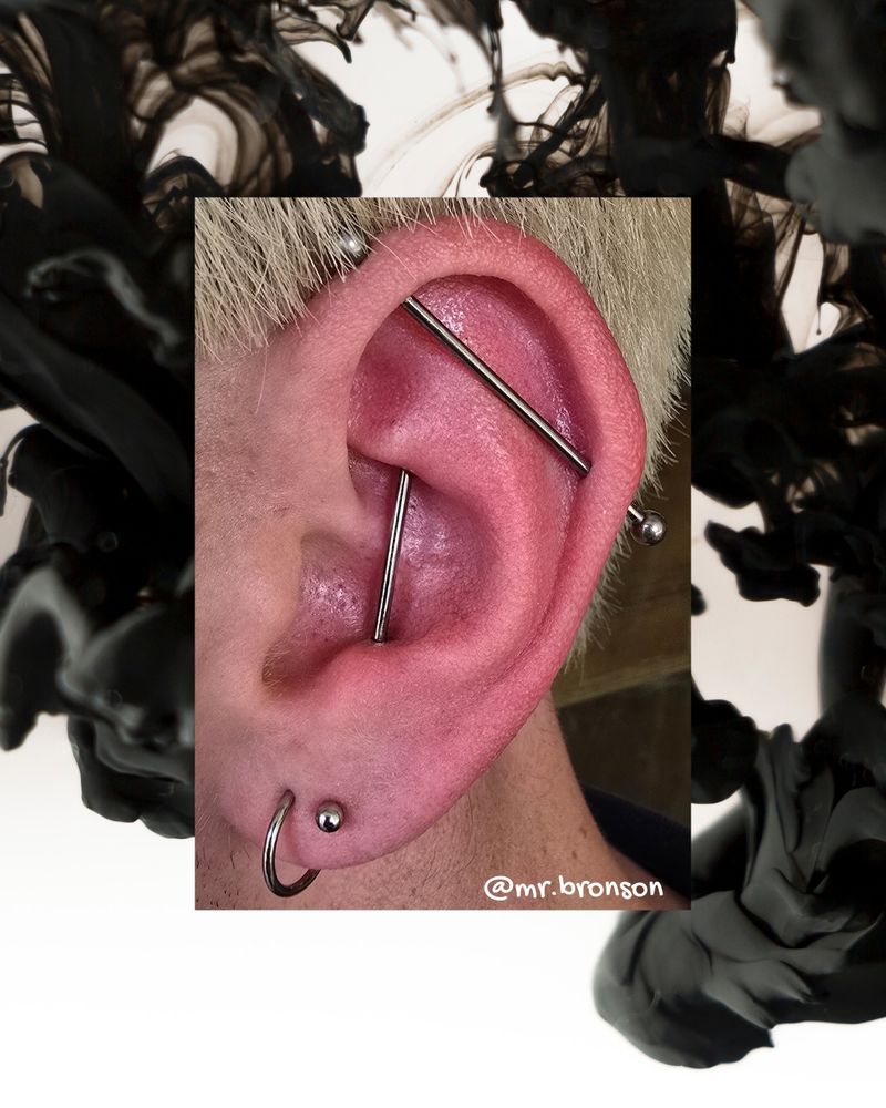 A close-up photo of an ear with two long pieces of jewelry and 2 lobe piercings, one with a ring and the other with a silver colored stud