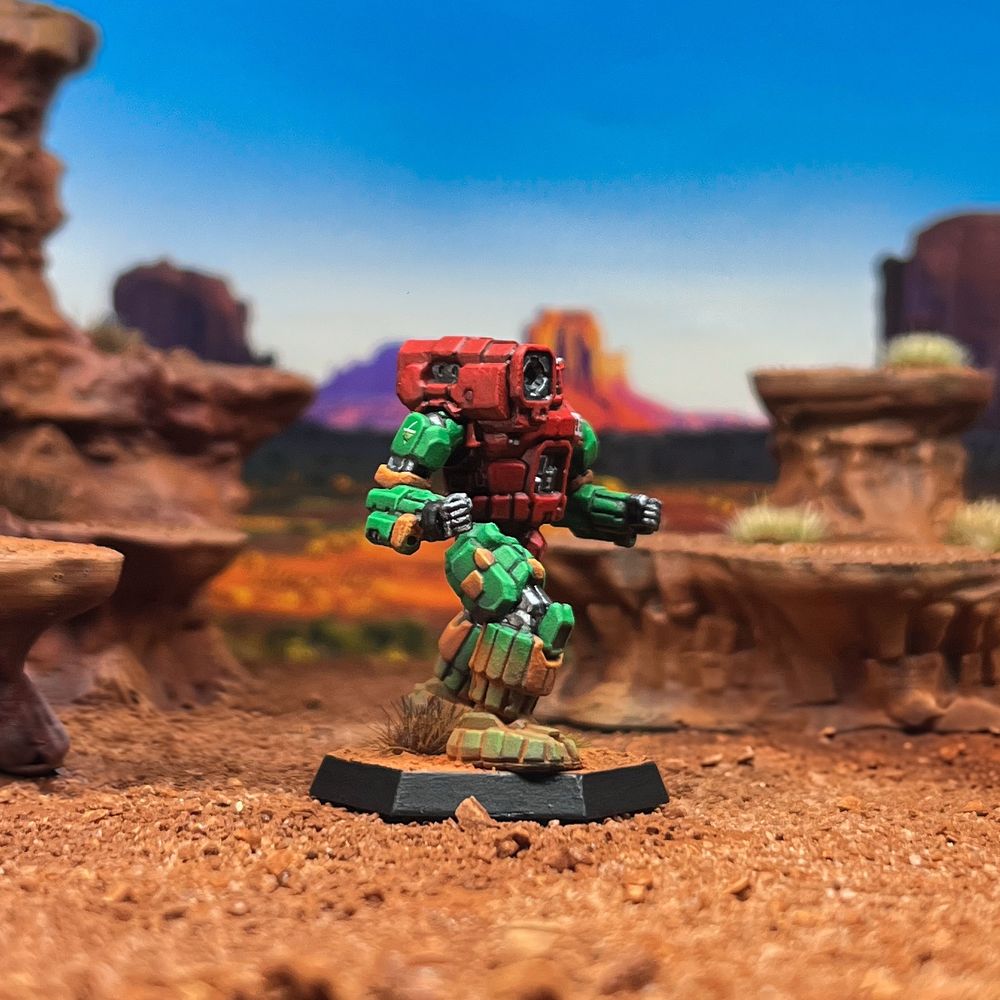 Right angle photo of a Hunchback mech painted in the 9th Sian Dragoons scheme of the Capellan Concentration. Red torso, green limbs, orange highlights. Its base is done in a badlands scheme. 