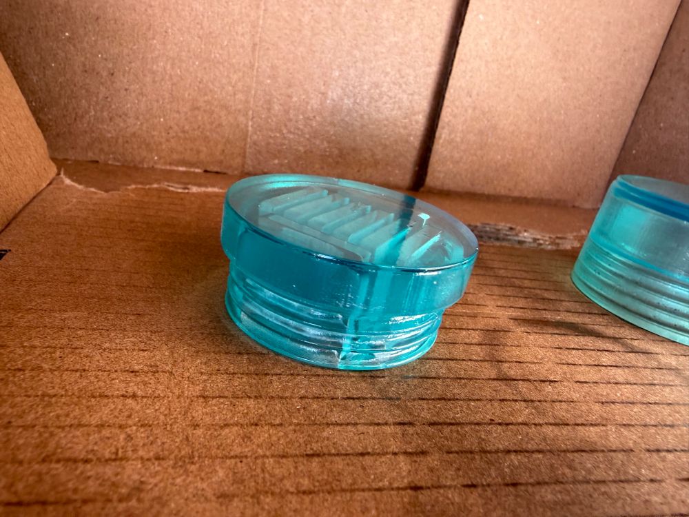 A transparent glossy blue half of a cylindrical threaded capsule that holds switch games in a cardboard box that looks slightly wet in places. There is another off to the right 