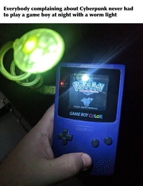 A purple game boy color with a worm light playing pokemon crystal being held by a single hand. The worm light spirals up a 2 or so inches above the screen lighting it up with a hot spot so bright you can’t see the game in that specific spot. 