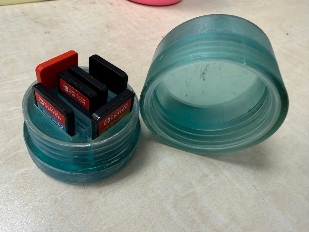 A ice blue semi transparent capsule on a white table with top removed and switch game poking out the top of slots on the bottom part of capsules 