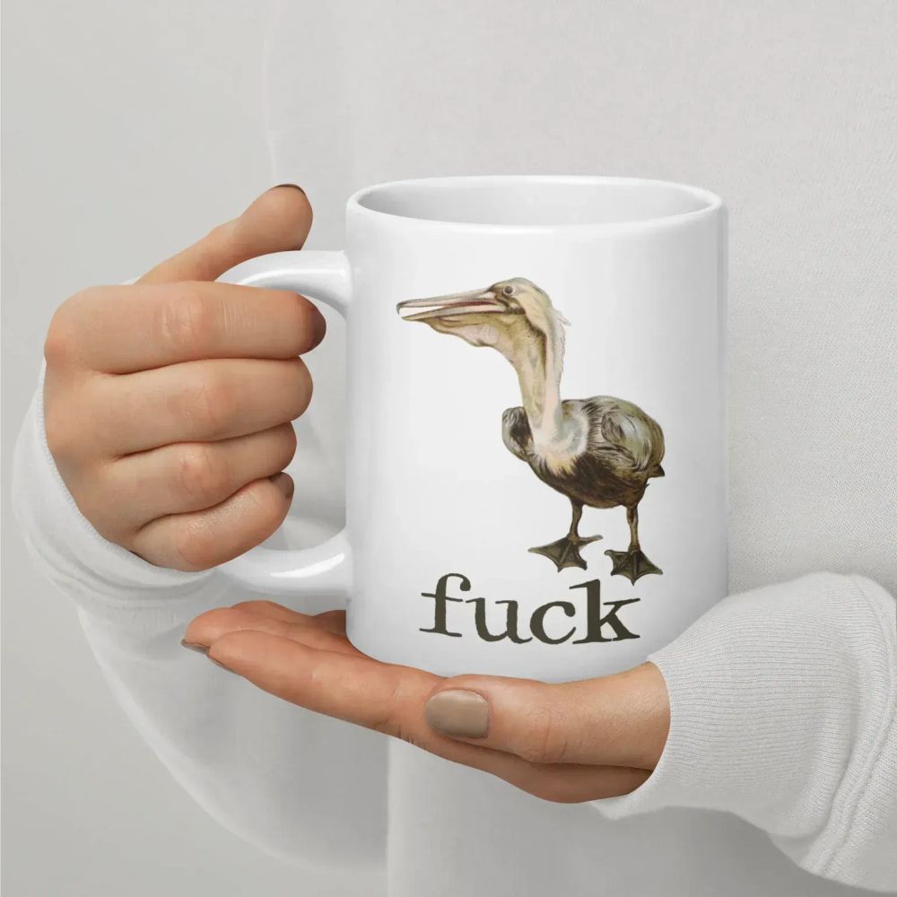 A photograph of a large coffee mug featuring a painting of a pelican above the word "fuck".