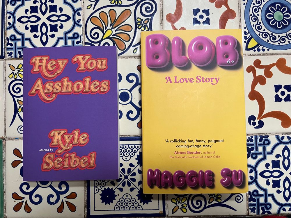 Two book - Hey You Assholes by Kyle Seibel and Blob by Maggie Su - sit atop a colourfully tiled coffee table.