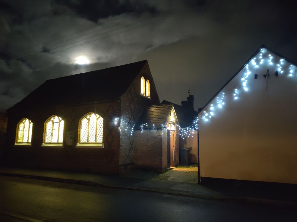 The village hall in the dark under a witch cloud sky. Festoon Christmas lights. 