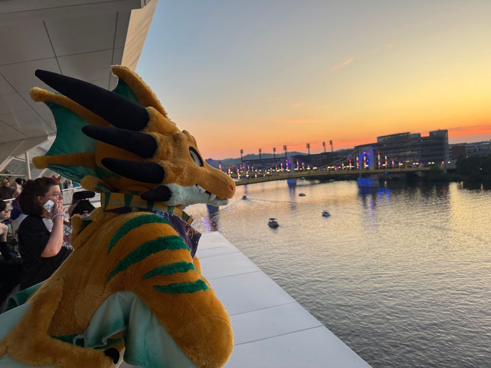 Setrahn the bronze dragon leaning on the fence of a balcony, looking pensively over the river, a bridge self-illuminated in the distance.