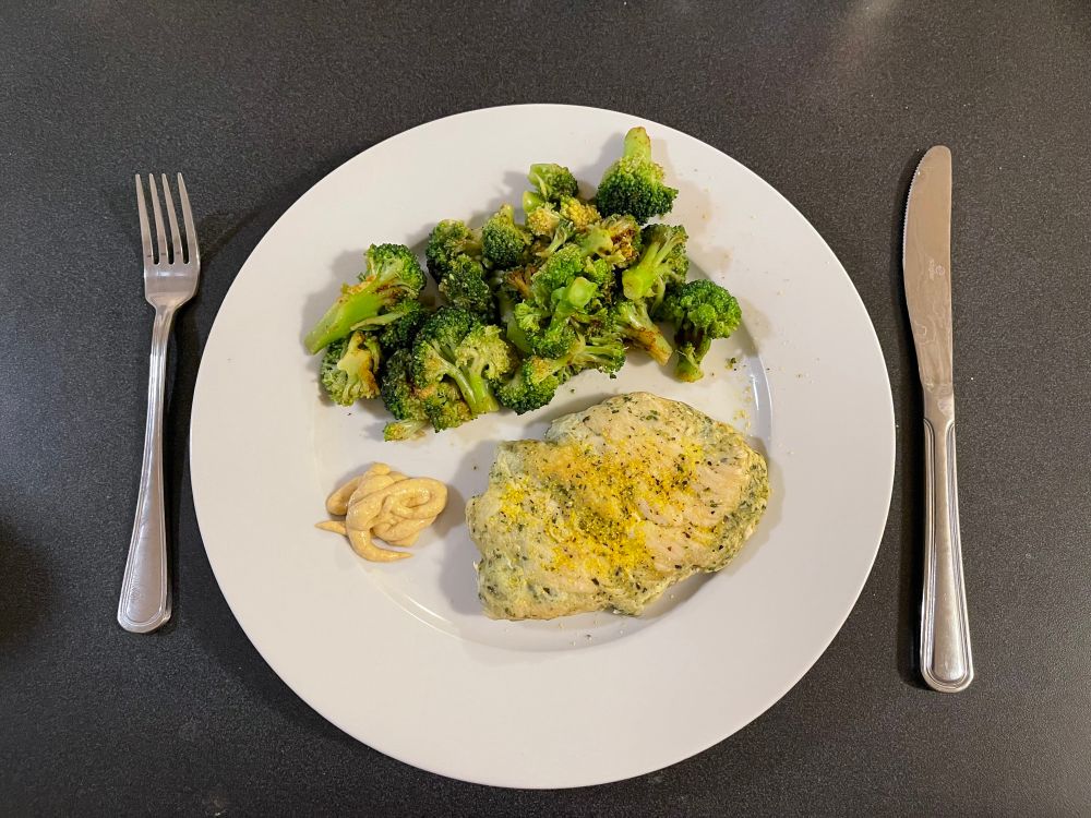 a plate with lots of broccoli, mustard, and chicken with a fork and knife by it