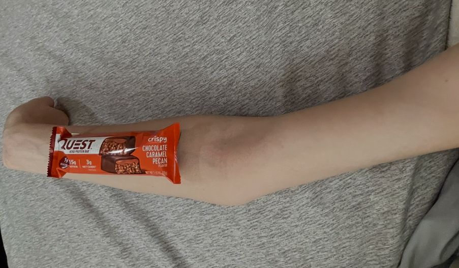 extended arm with DELICIOUS 170 kcal quest chocolate caramel pecan bar on top