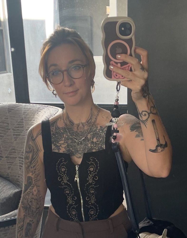 Me taking a mirror selfie in a black top with a half done tattoo cover up on my chest.