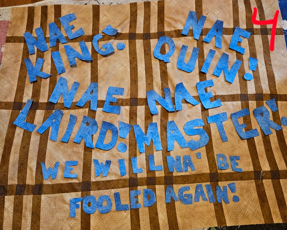 All of these are Tan and brown fabric pieced together to look like tartan. Laying in it are blue block letters that spell out "Nae King! Nae quin! Nae Laird! Nae master! We willna' be fooled again!"

For 4: the Nae phrases are one in each corner with we willna' In two lines on the bottom centered