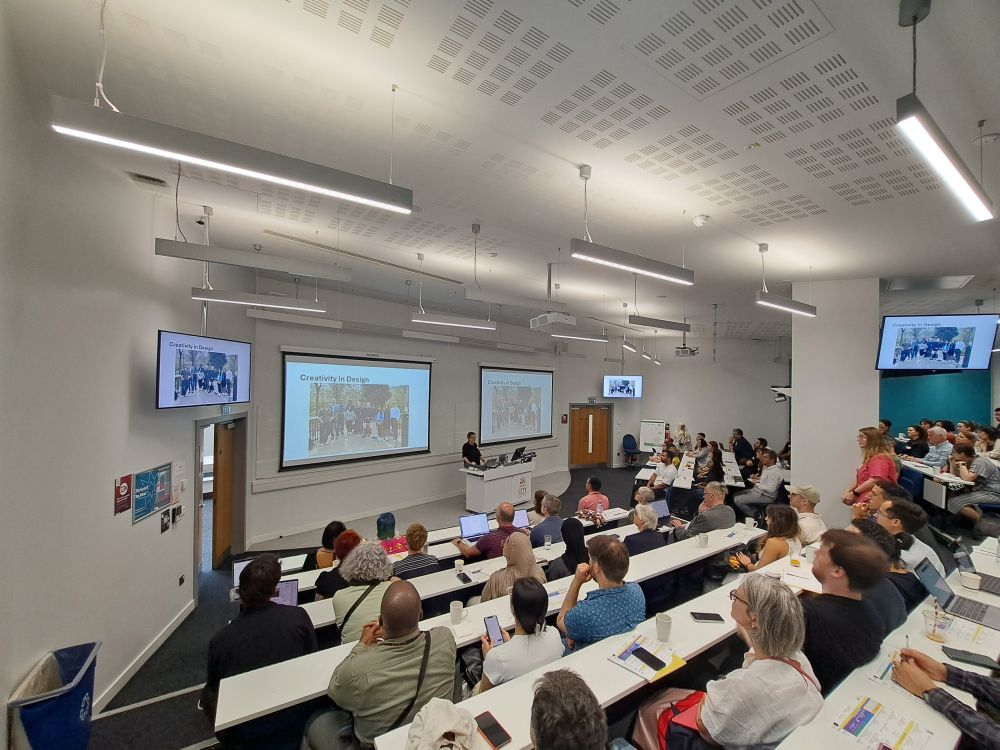 Stephanie Wilson in full capacity lecture theatre, 5 screens (2 large ones; 3 smaller ones) with slides