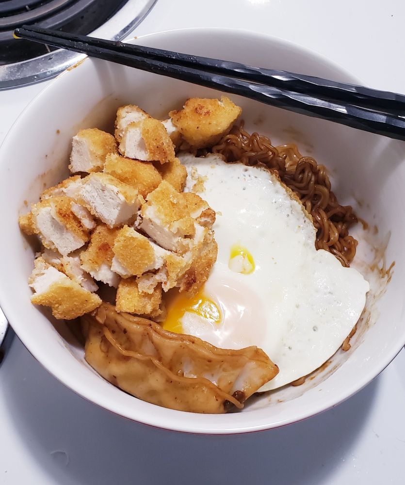 the prepared noodles and potstickers with fried chicken and an egg topping them