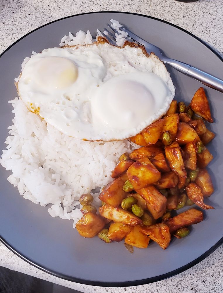 a bed of white rice is topped with two fried eggs, and a red medley of teriyaki-gochujang pineapple and chicken, speckled with roasted edamame 