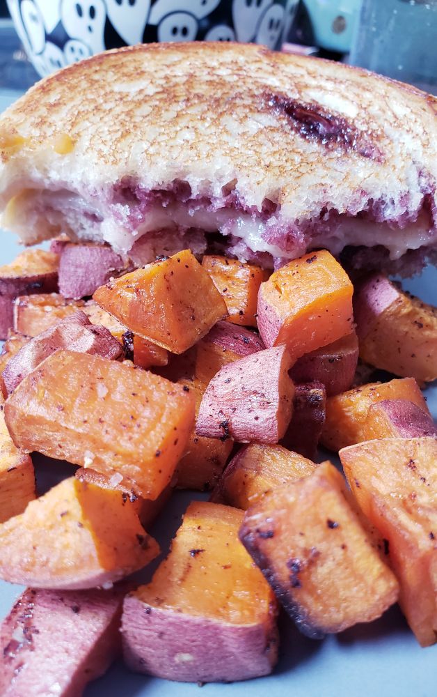 a golden grilled cheese with bits of purple blackberry jam, over a pile of roasted orange sweet potato.
