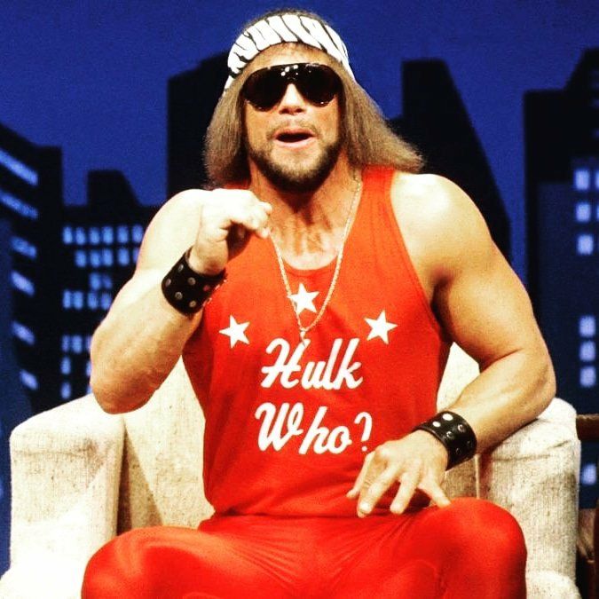 Macho Man Randy Savage in a zebra headband and black shades. He is sat on a chair holding a microphone and looks to be mid-speech, in an all-red ensemble, his shirt detailed with 3 white stars and text that reads "Hull Who?"