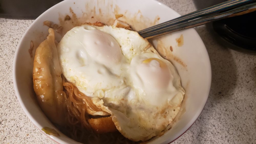a bowl of yakisoba Buldak noodles topped with egg and gyoza with diced chicken breast