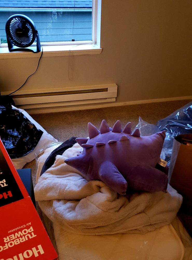 Gengar is flopped over on a pile of cushions , face down, with a fan blowing in
