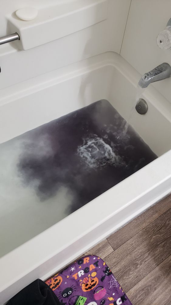 a bathtub being filled with water, with a roilinv bath bomb that looks like black ink dispersing into the tub and turning the water dark