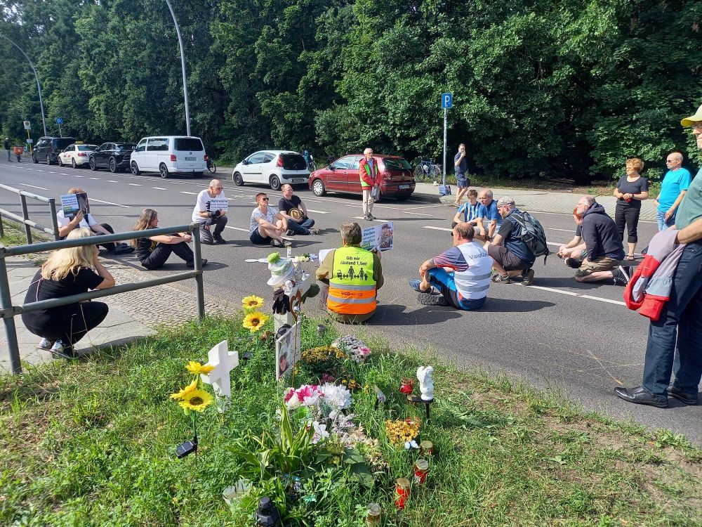 Mahnwache mit verschiedenen Personen die für eine Schweigeminute auf der Fahrbahn sitzen.