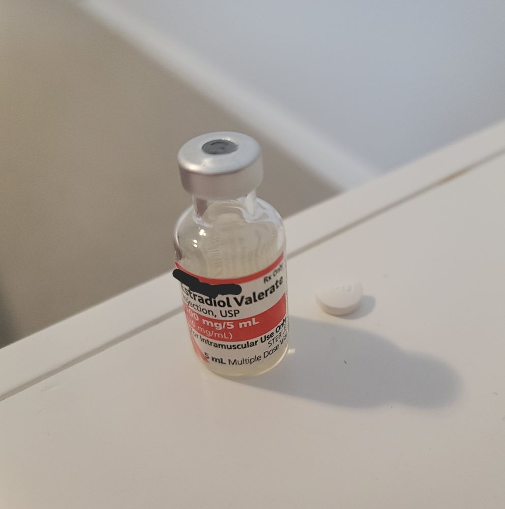 vial of estradiol valerate 100mg/5mL and half of a 100mg spironolactone pill