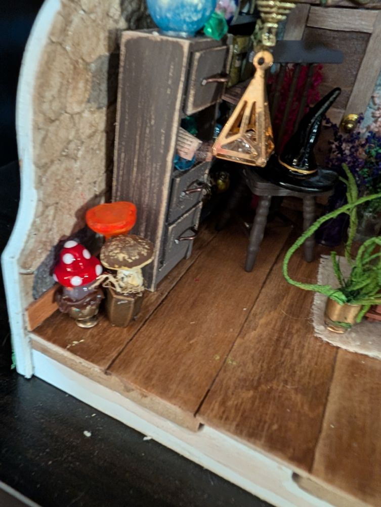 A closeup on three mushroom planters - one red capped and white dotted, one brown cap and cream coloured stem, one red lobster mushroom) in a 1:12 scale diorama.