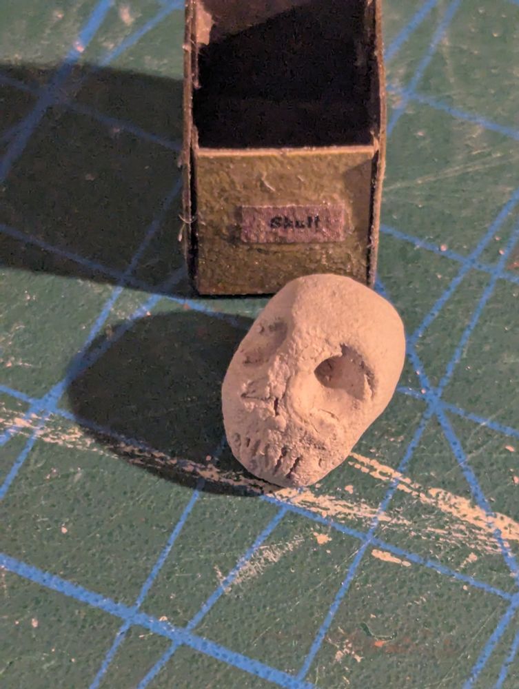 The skull is... Not a very good skull. But it's in a box that has a skull label, so that's what it is. What's more, no one actually plays with my dollhouses, so no one will know that there is a skull in a box labeled skull, also shown, on a cutting mat with a 1cm grid to show scale. The actual radius of the skull is a little less than 4mm