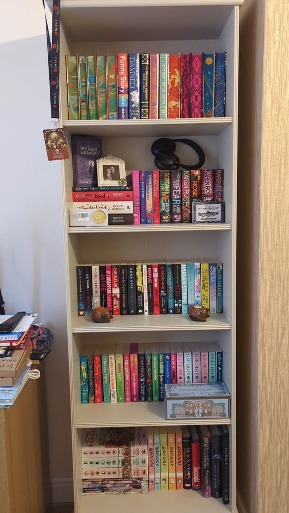 Kit's new bookcase - a grey wooden bookcase with five shelves filled with books. Special editions are on the top shelf, with crime novels on the second, thrillers on the third, romance on the fourth, and graphic novels on the bottom shelf