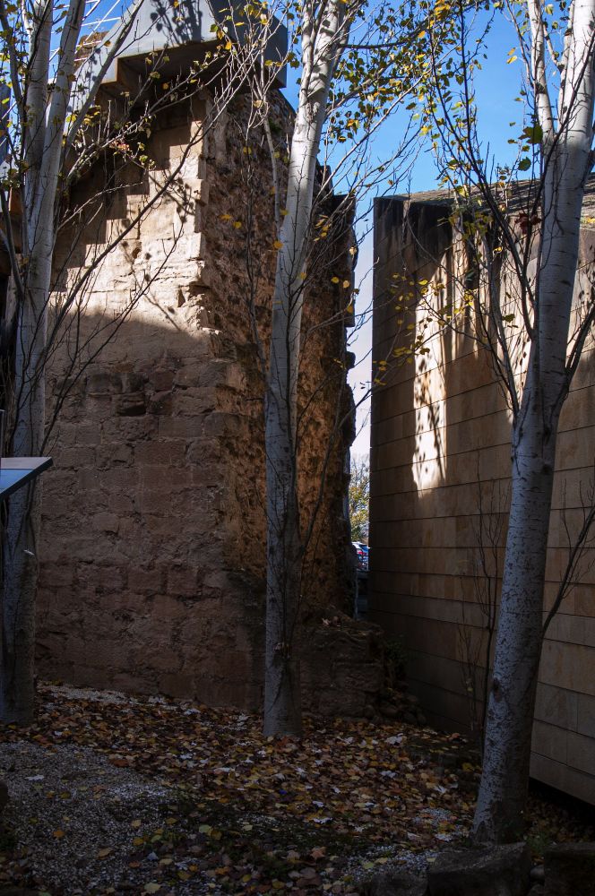 Interior courtyard of the defensive tower museum. A group of birch trees grow near the old city wall, part of it now missing. A modern building, part of the museum, and made to imitate where the wall would be, sits near it.