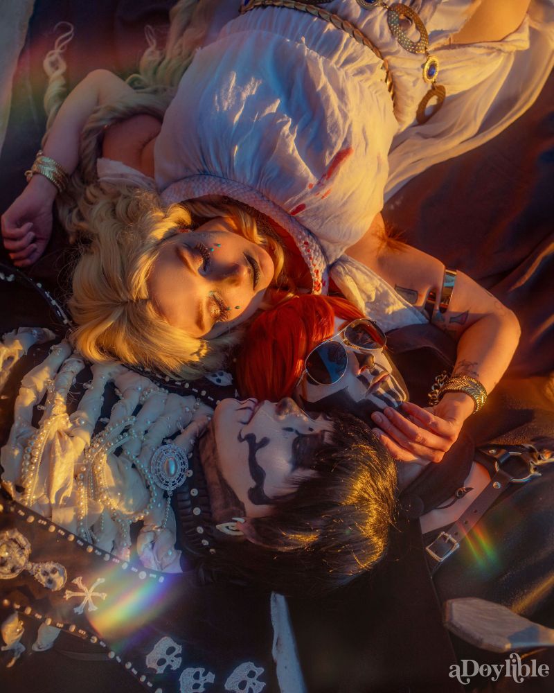 Alecto, Gideon Nav, and Harrowhark Nonagesimus all laying on the ground together, heads all towards the center. Alecto caresses Gideon's chin, Harrow's head leans against Gideon. They are lit by the golden hour sun framed by soft prisms casting rainbows around them. 