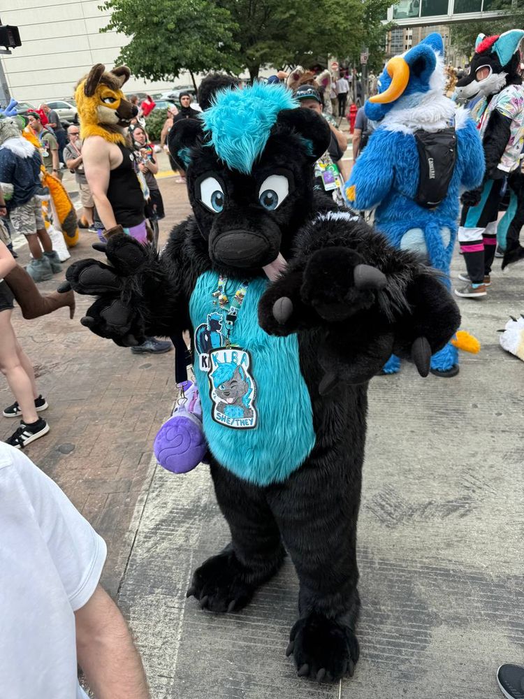Kiba, a blue and black skunk fursuiter, points at the camera with one paw