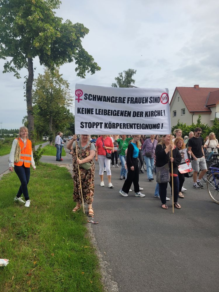 Menschen halten ein Demoplakat mit der Aufschrift "Schwangere Frauen sind keine Leibeigenen der Kirche! Stoppt Körperenteignungen!"