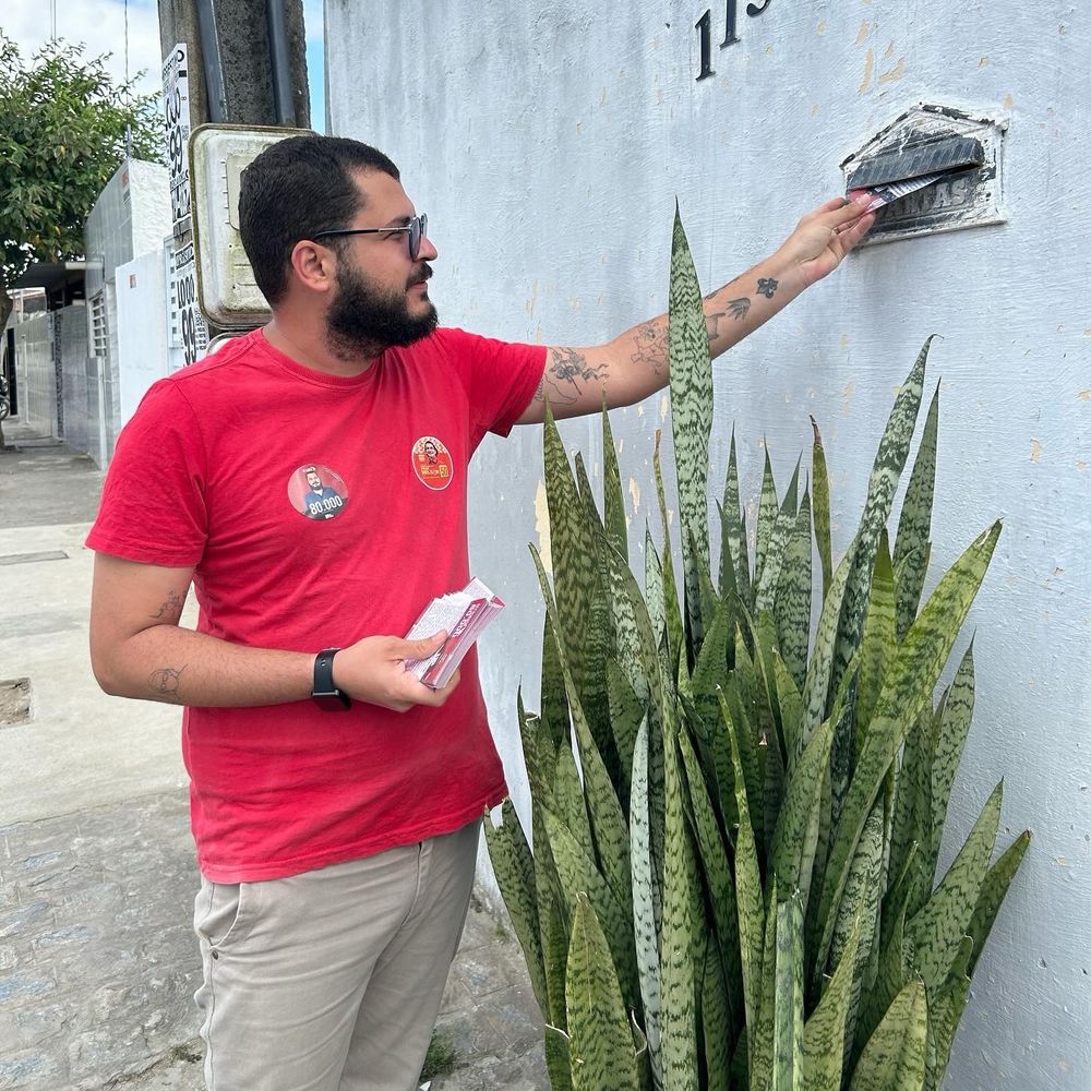 Homem colocando panfleto dentro de uma caixinha de correspondência.