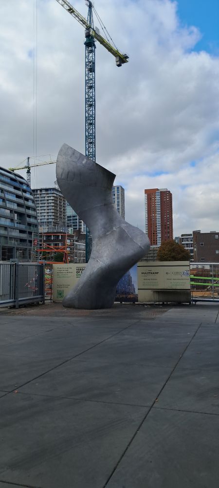 A large metal sculpture of a foot in front of a building site in a city