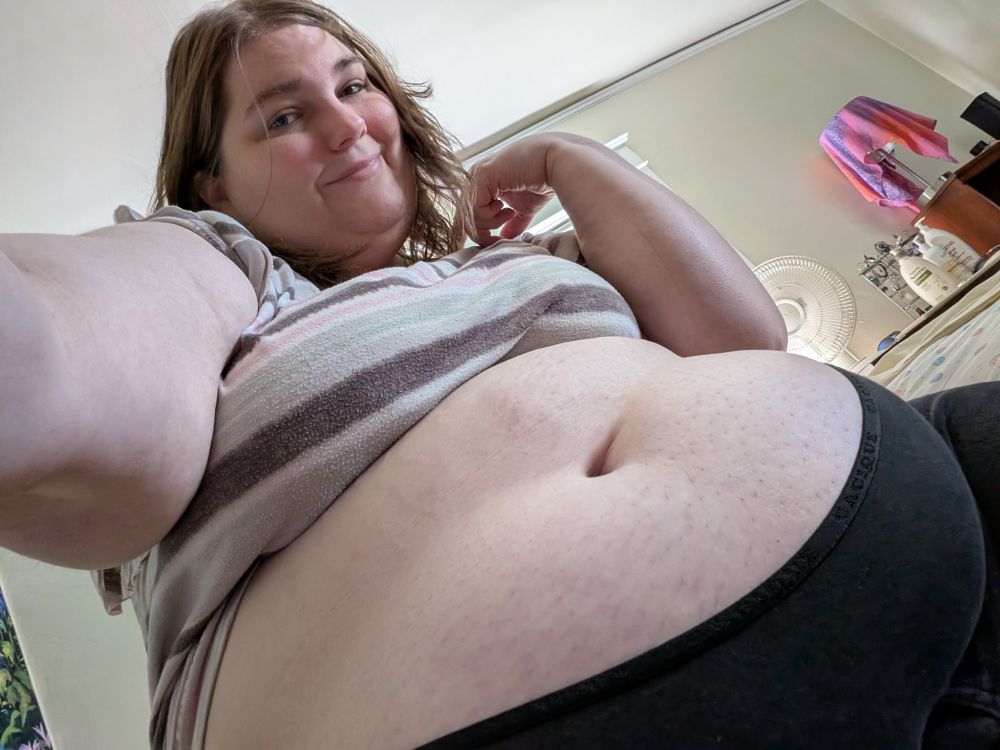 Low angle selfie showing my big fat SSBBW belly while I look at the camera with a slightly flirtatious smile and hopeful eyes 