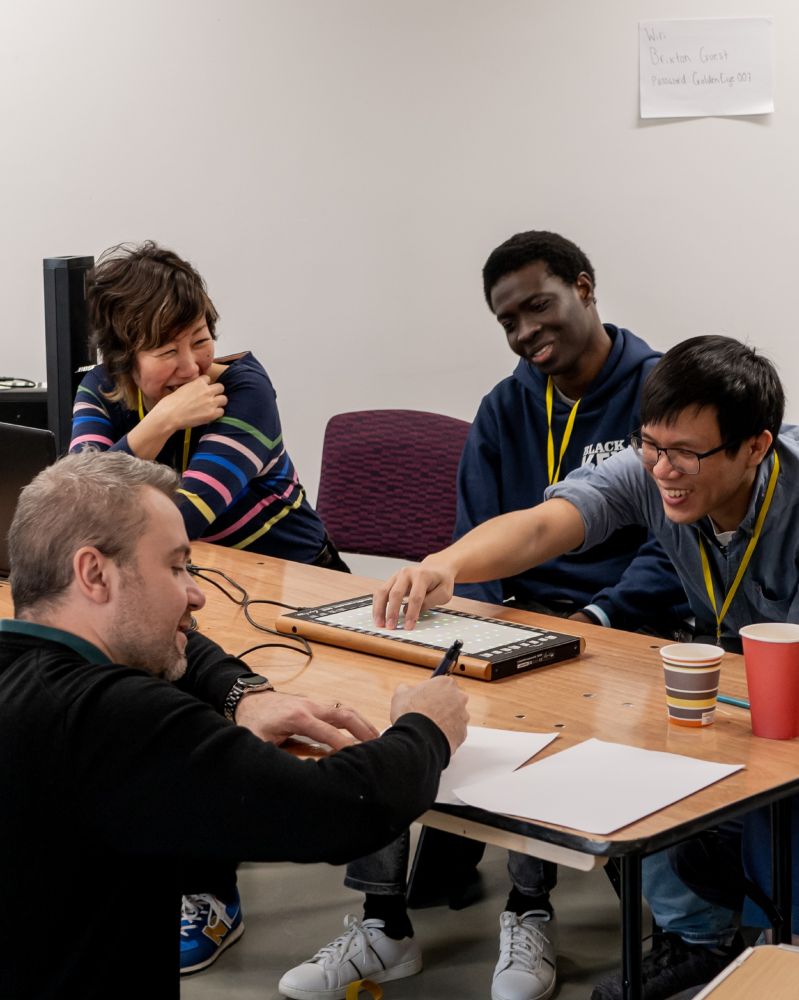 Photo of four people seated around a table, enjoying exploring the Linnstrument together.