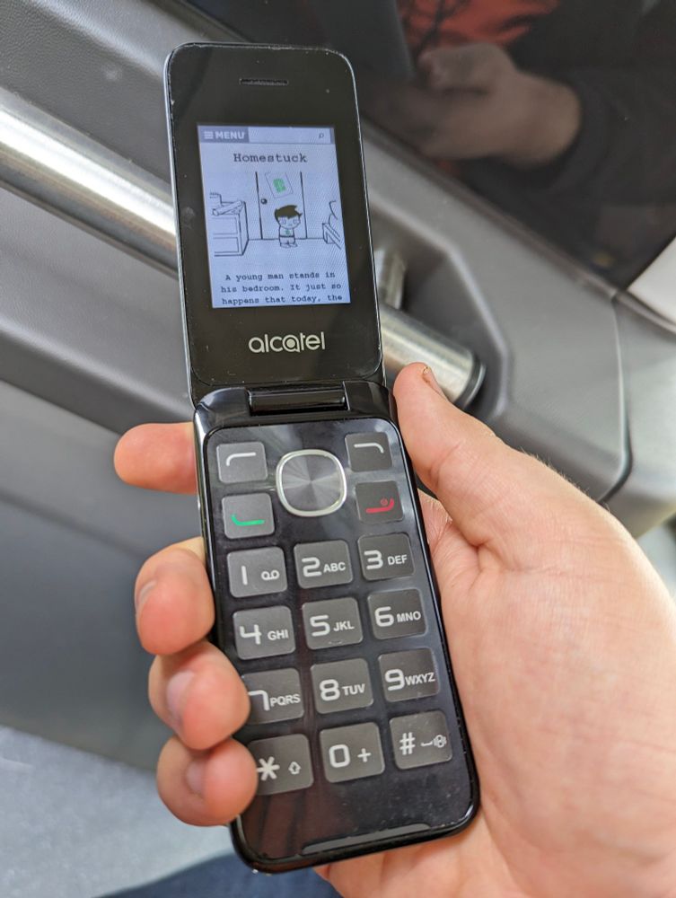 Photo of an old alcatel flip-phone displaying the first page of the webcomic Homestuck in its browser.