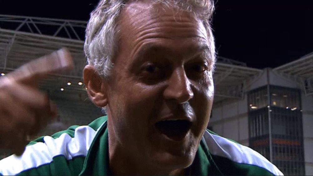 a man with gray hair and a green and white shirt is screaming with his mouth open