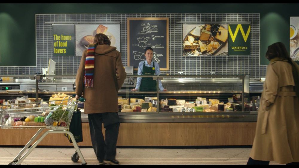 A middle-aged man wearing a stripy coloured scarf checks out the deli at Waitrose.