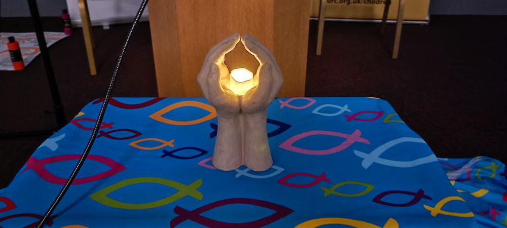 Electric tea light on plaster hands on a URC tablecloth. 