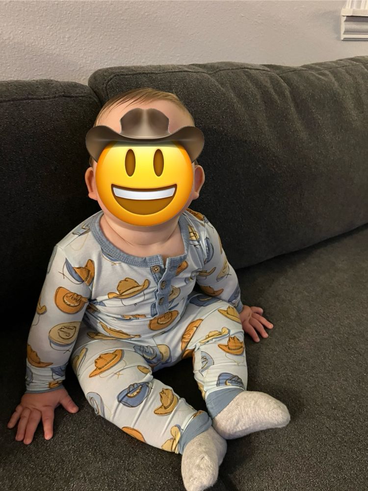 Baby in pajamas with cowboy hats on them, face covered by an emoji