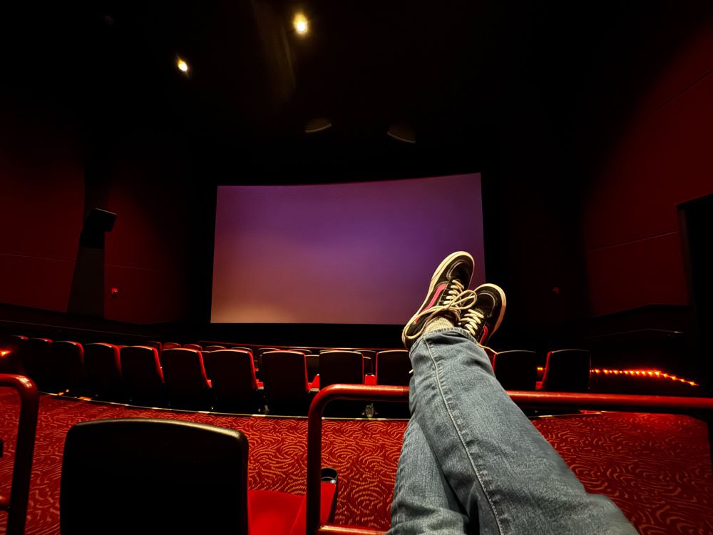 A pair of legs/feet up on a railing in an empty movie theater