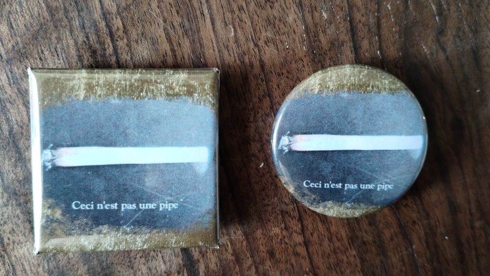 One square and one round button depicting a burning joint with the caption "Ceci n'est pas une pipe." on a black and gold background.