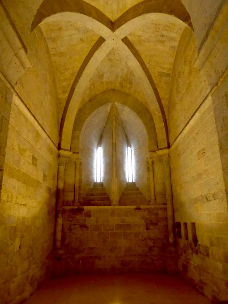 La luz que entra por una estrecha ventana partida ilumina en tonos amarillos una sala estrecha. Arcos se cruzan en el techo 