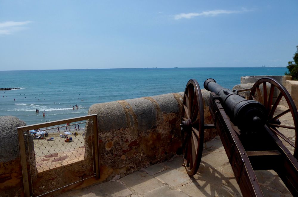 Primer plano de un cañón antiguo en una torre de vigilancia de la costa. Mar azul y cielo azul. Dos barcos en el horizonte.