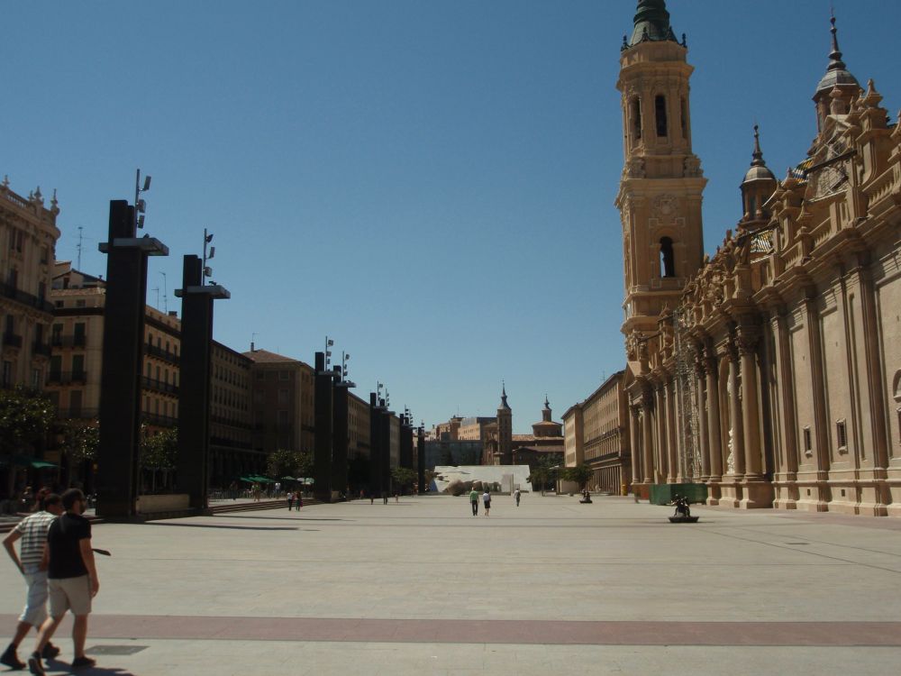 Una gran plaza. A la derecha la Basílica del Pilar. A l izquierda diversos edificios. Cielo azul