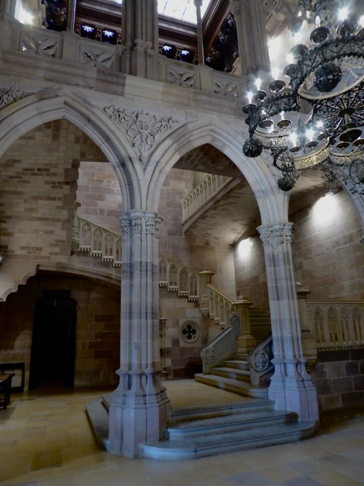 Sala de estilo neogótico. Una arcada da paso a una escalinata. A la derecha una lámpara cuelga del techo.