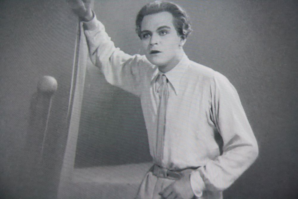 Freder is visibly wearing stage makeup with darkened lips and eyeliner while leaning on a wall.