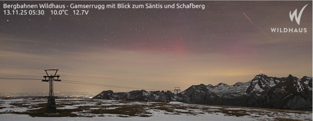webcam picture from muntain top with snow covered mountains in back.... and some faint aurora in the sky in pink