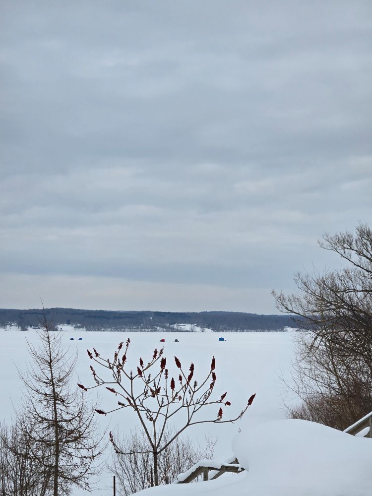 Frozen lake doted with a few ice fishing tents in the distance under an overcast sky.